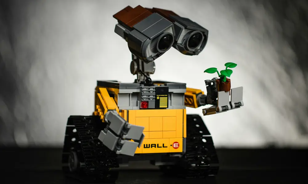 A black and yellow toy robot holding a toy plant. Written on the robot are the words wall-E.
