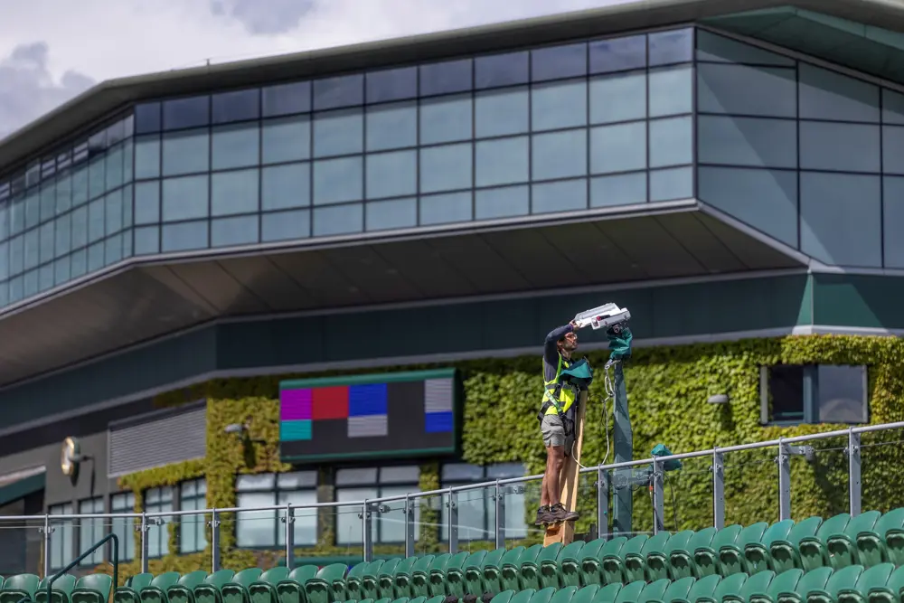 A technician securing a camera above the back row of seats, with Wimbledon's centre court building in the background.