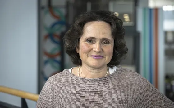 Penny has curly dark hair and wears a taupe jumper, she is smiling at the camera.