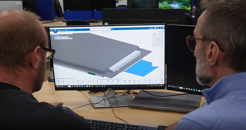 Image shows the back of two men's heads, both wearing glasses, looking at a computer screen that shows them designing a solid-state battery