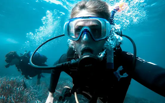 Close up of a man underwater, breathing through scuba gear.