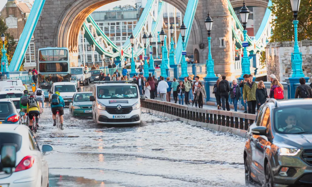 Cars and cyclists traverse through surface water on the approach to Tower Bridge