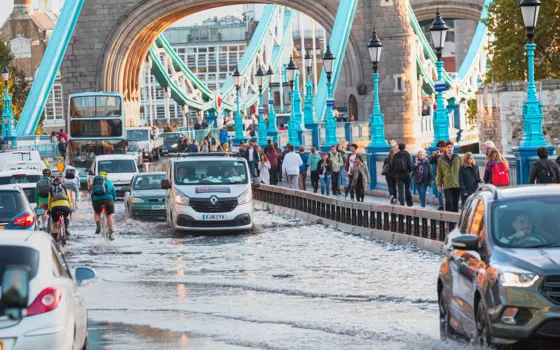 Cars and cyclists traverse through surface water on the approach to Tower Bridge