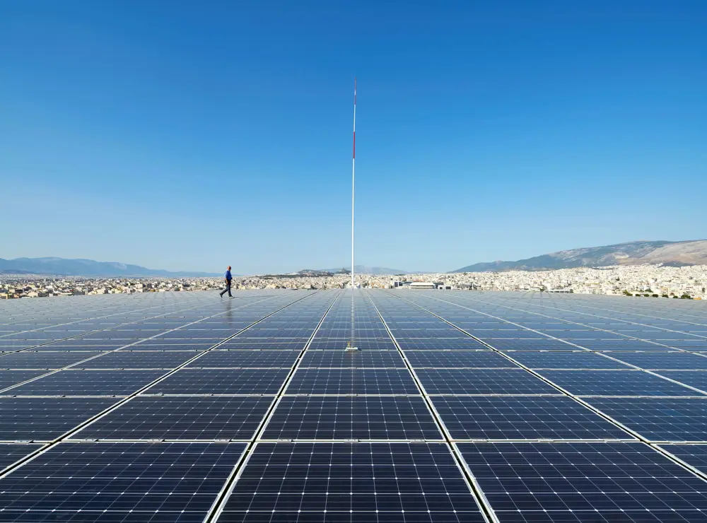 A person in the background walking among lots of solar panels. 