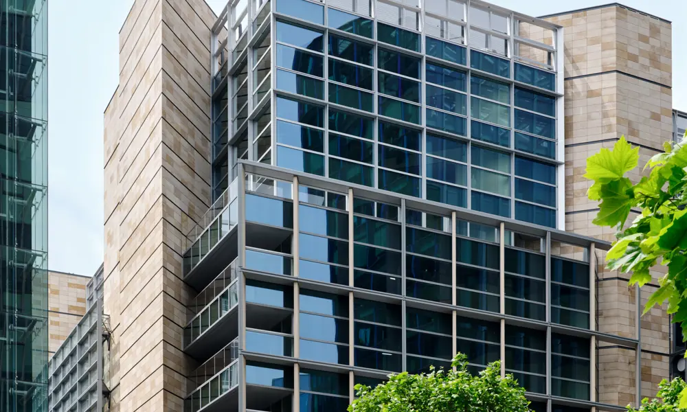 The tall Triton Square building in the UK with trees in the foreground and people sitting on concrete slabs.