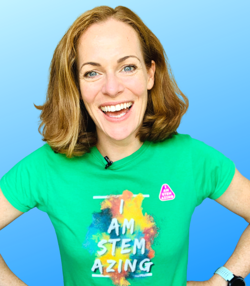 A woman in a green t-shirt with shoulder-length hair smiles at the camera with her hands on her hips, against a blue background