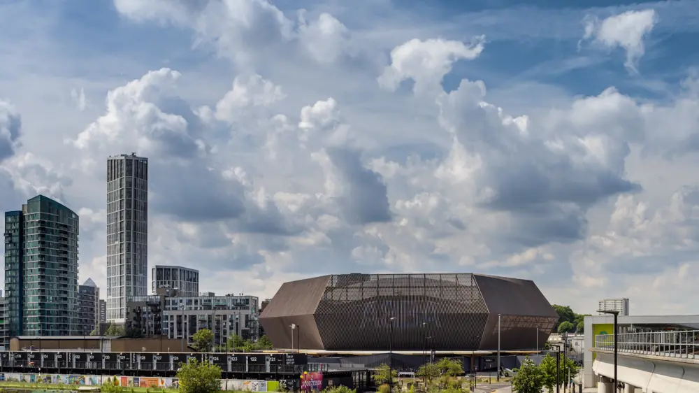 A wooden framed stadium seen next to skyscrapers with rolling clouds on a bright day