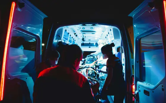 Emergency response professionals wearing masks loading the back of an ambulance with a stretcher at night.
