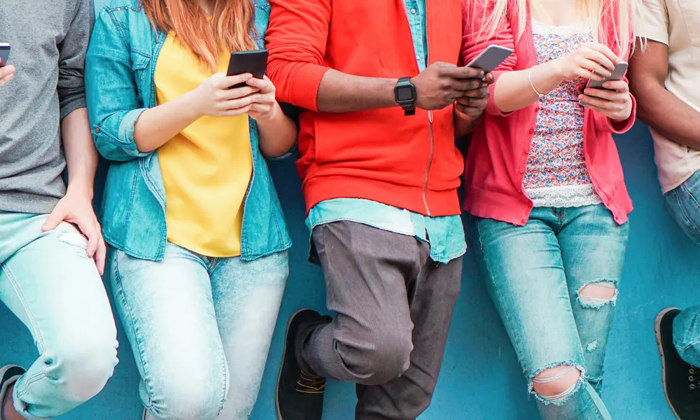 Five people from the neck down holding mobile phones. 