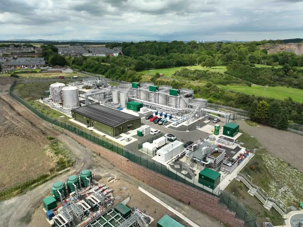 An overhead image of a wastewater treatment works showing a number of silver steel tanks and green cube structures. The plant is surrounded by fields and trees