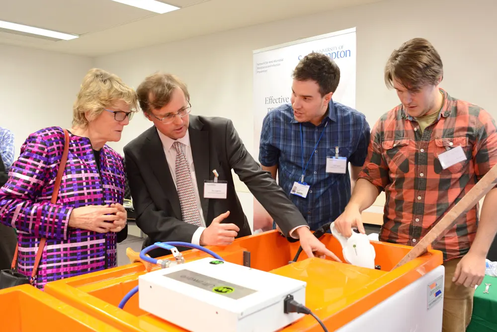 Professor Timothy Leighton standing next to Professor Dame Sally Davies behind a demonstration of the StarStream device, explaining how it works.