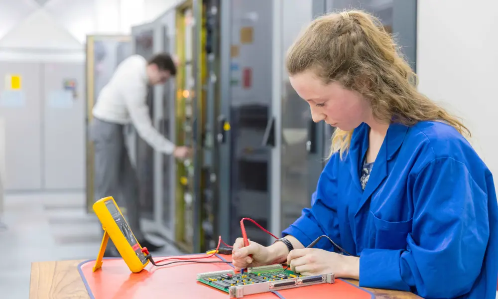 A young female engineering apprentice works on a circuit board.
