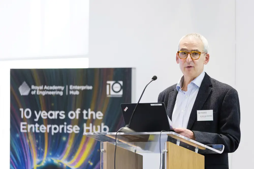 A man with tortoise shell glasses speaking at a lectern.