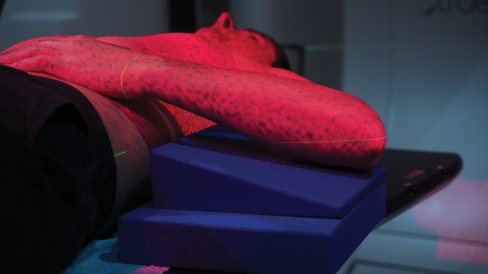 A patient lying down with red light covering their body to accurately position radiotherapy treatment. 