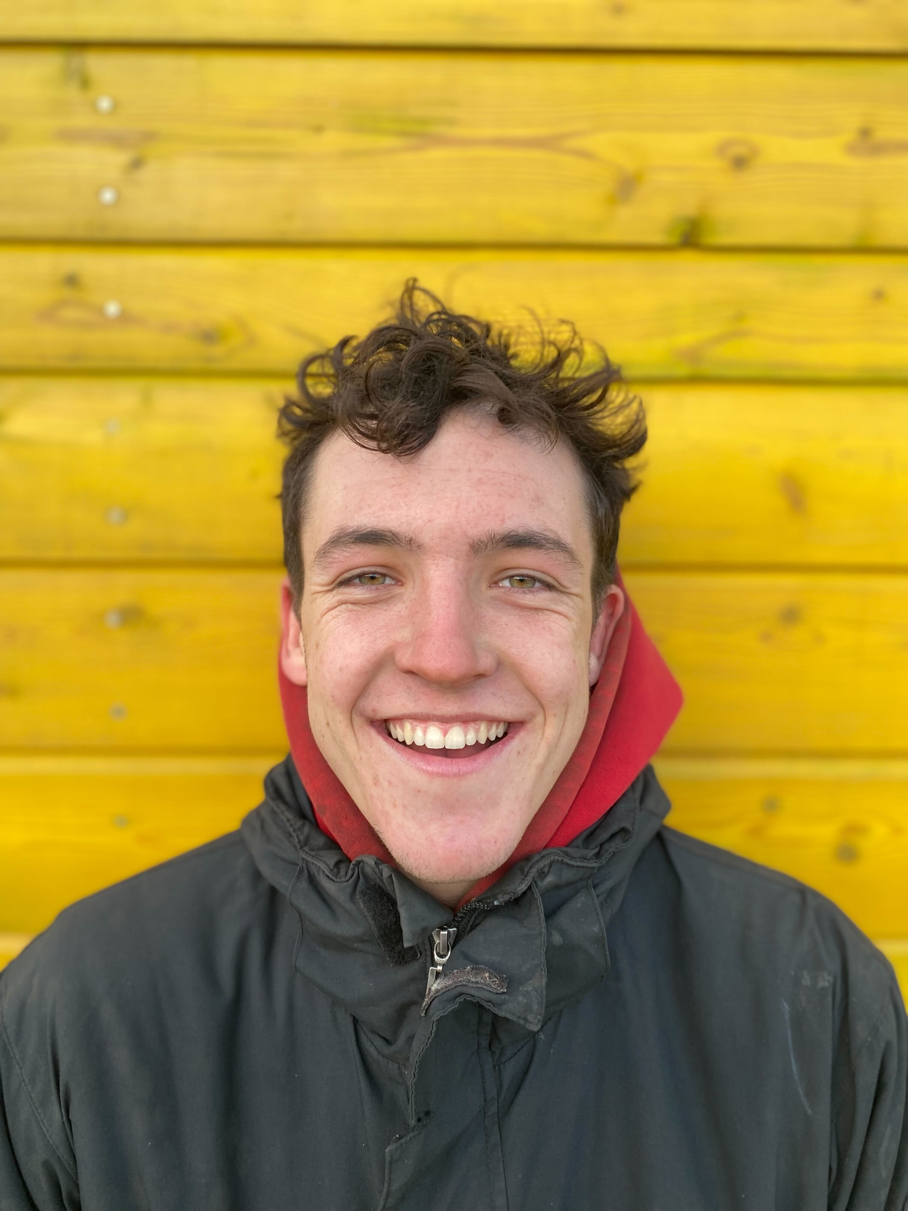 A playground engineer smiling, standing in front of a yellow wall.