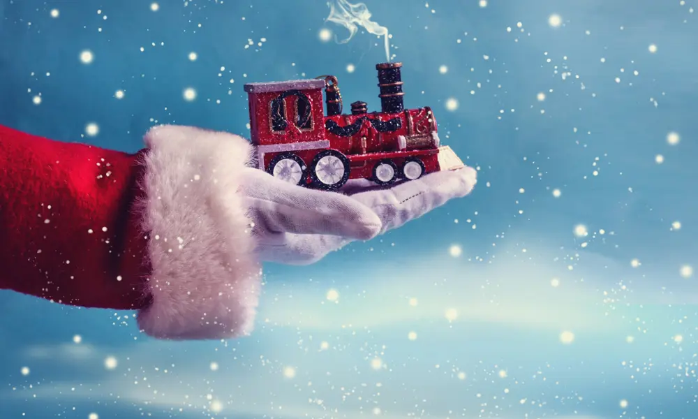 A hand with a red and white fluffy sleeve and white glove holding a toy train with steam coming out the top.