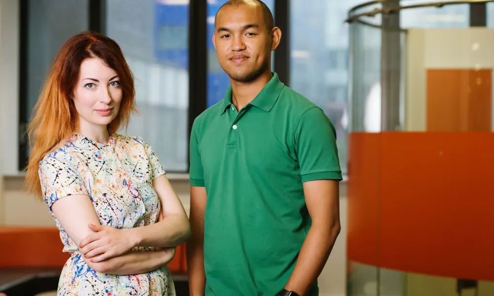 A woman in a colourful dress stands with her arms crossed opposite a man wearing a green t-shirt