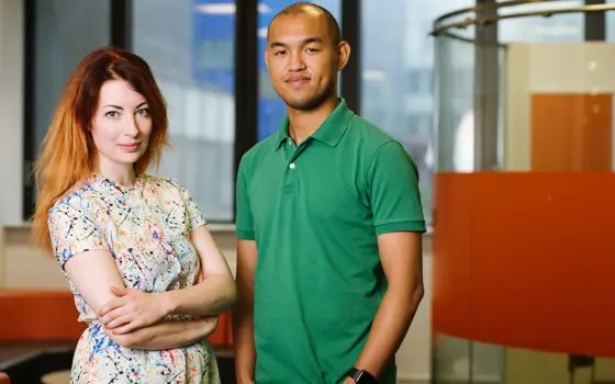 A woman in a colourful dress stands with her arms crossed opposite a man wearing a green t-shirt