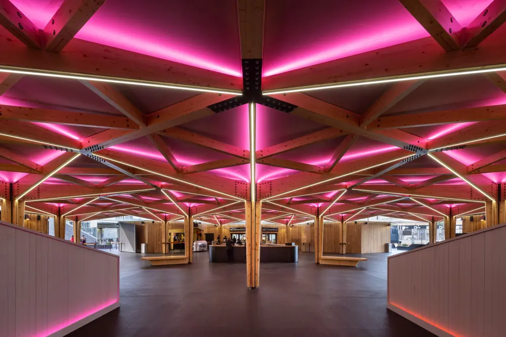 Pink glowing LED lights illuminate an intricately patterned timber frame in the lobby by a ticket desk