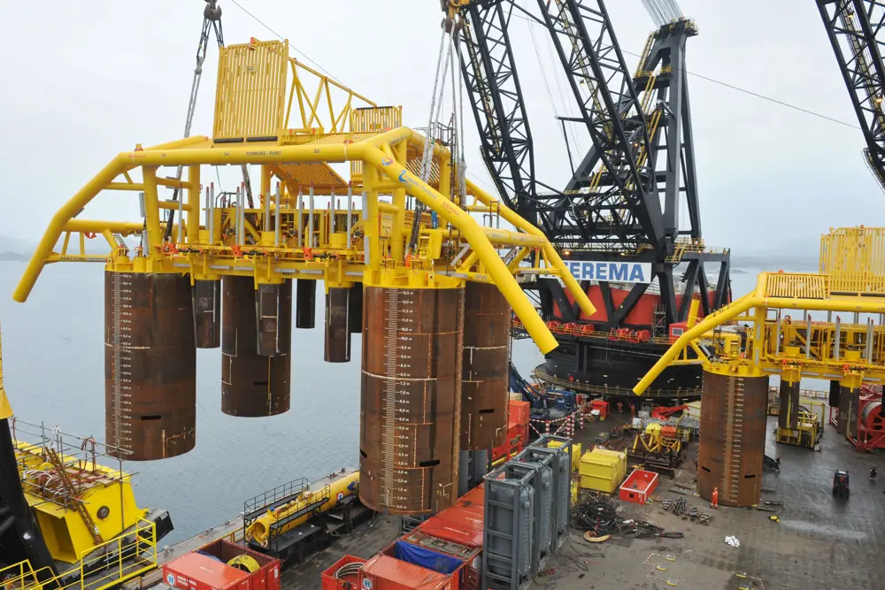 A crane lifting large metal cylinders with the ocean in the background. 