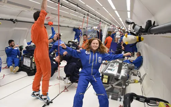 A woman floating in a space suit with her hair spread around her in the hold of a plane during parabolic (zero gravity) flight