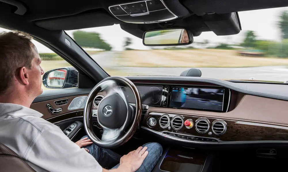 A man sitting in a moving car autonomous vehicle, with his hands on his lap.