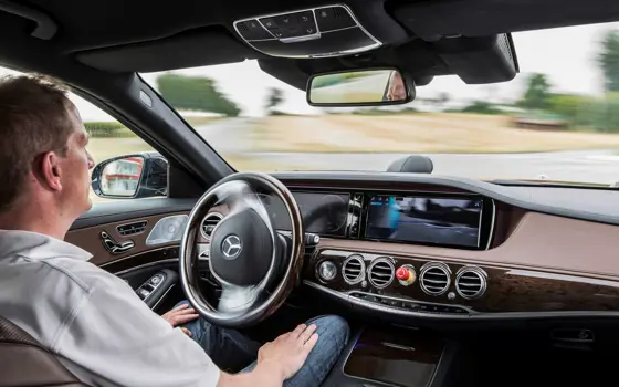 A man sitting in a moving car autonomous vehicle, with his hands on his lap.
