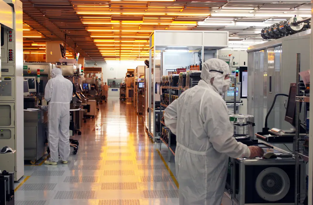 Two scientists wearing cleanroom suits, working in a laboratory that develops semiconductor devices and processes.