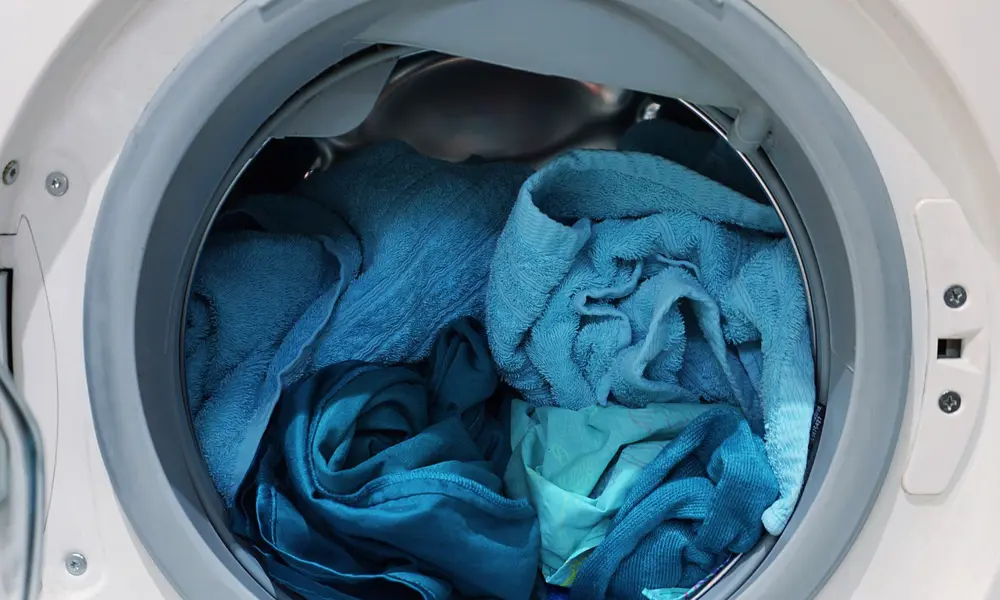An open washing machine appliance, containing a mixture of different blue fabrics.