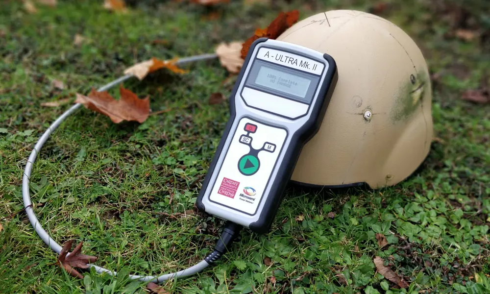 The A-Ultra handheld device resting against a helmet displaying the words '100% complete no damage' on it's screen.