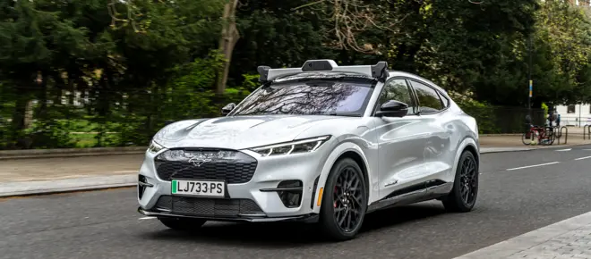 An electric car driving along a tree-lined road, with a rig of cameras on top.