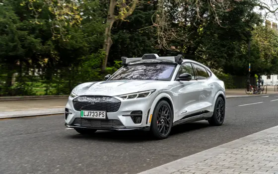 An electric car driving along a tree-lined road, with a rig of cameras on top.