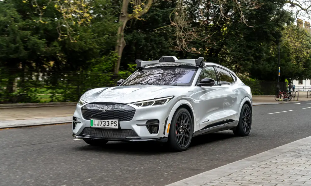 An electric car driving along a tree-lined road, with a rig of cameras on top.