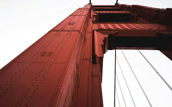 A worms-eye view of a red steel tower of the Golden Gate Bridge on an overcast day.