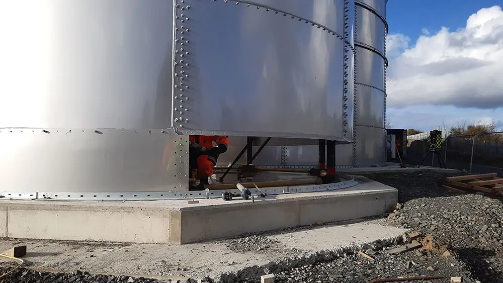 The bottom of a steel tank showing a person wearing high vis  crouching down through a gap