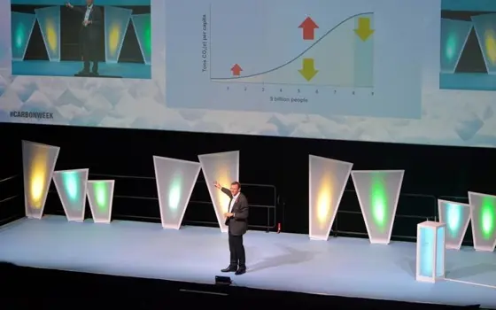 A man onstage in a dark suit, presenting to an audience in front of slides.
