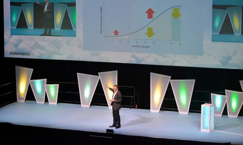 A man onstage in a dark suit, presenting to an audience in front of slides.
