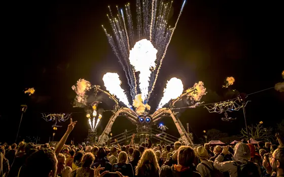 A crowd at Glastonbury festival watching the Arcadia Spider shoot out flames at night. 