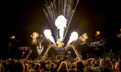 A crowd at Glastonbury festival watching the Arcadia Spider shoot out flames at night.