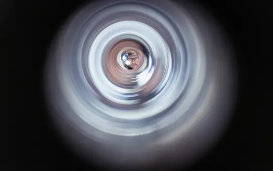 Aman wearing glasses shines a torch through a cylindrical object, looking towards the camera