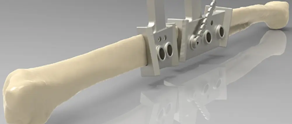 A long bone on a flat surface containing the AM-produced cutting-and-drilling metal guide attached to it.