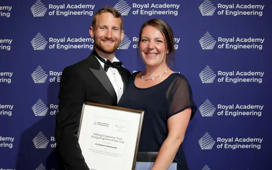 A man and woman in black tie, posing for a photograph; the man is holding a certificate