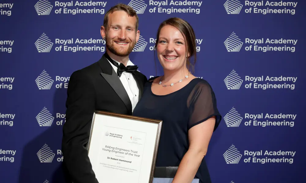 A man and woman in black tie, posing for a photograph; the man is holding a certificate