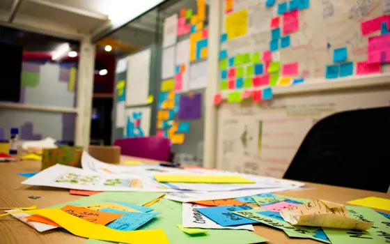 A desk filled with different coloured post-it notes with a whiteboard and more post-it notes in the background. 